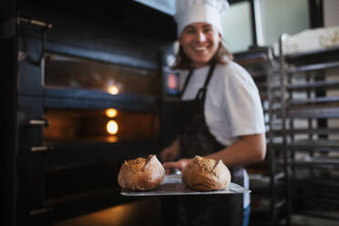 Glücklicher junger Bäcker mit frischem Brot in einer Bäckerei. - HPIF10656