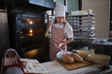 Glücklicher junger Bäcker mit frischem Brot in einer Bäckerei. - HPIF10657