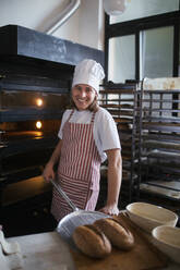 Glücklicher junger Bäcker mit frischem Brot in einer Bäckerei. - HPIF10660