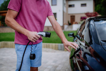 Ein Mann hält ein Stromversorgungskabel an einer Ladestation für Elektrofahrzeuge. - HPIF10688