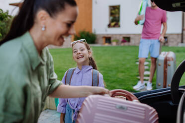 Eine glückliche Familie bereitet sich auf den Urlaub vor, indem sie ihre Koffer in den Kofferraum packt, während ihr Elektroauto aufgeladen wird. - HPIF10714