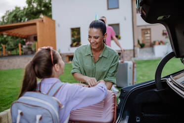Eine glückliche Familie bereitet sich auf den Urlaub vor, indem sie ihre Koffer in den Kofferraum packt, während ihr Elektroauto aufgeladen wird. - HPIF10716