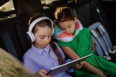 Kleines Mädchen schaut in digitale Tablet und hören Musik, ihre Schwester einschlafen während Familienausflug im Auto. - HPIF10719