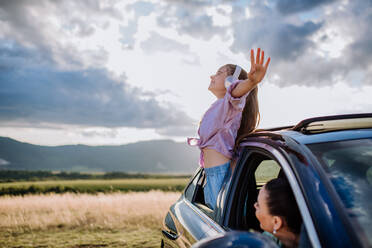 Little girl with a headphones standing and leaning out of the car window during the ride. - HPIF10725