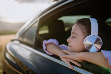 Kleines Mädchen mit einem Kopfhörer, das während der Fahrt aus dem Autofenster schaut. - HPIF10726