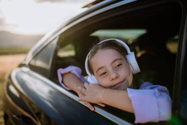 Kleines Mädchen mit einem Kopfhörer, das während der Fahrt aus dem Autofenster schaut. - HPIF10727