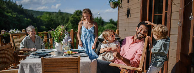 Drei Generationen Familie, die Spaß an Grillparty Abendessen auf der Terrasse, Menschen sitzen am Tisch auf der Terrasse mit Grill. - HPIF10734