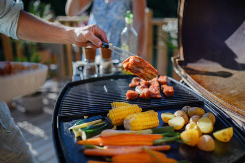 Ein unkenntlicher Mann grillt Rippchen und Gemüse auf dem Grill während einer Familien-Sommergartenparty - HPIF10737