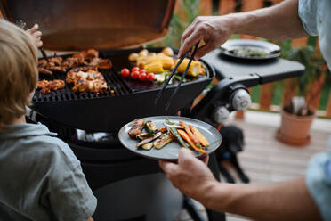 Ein nicht erkennbarer Vater mit seinem kleinen Sohn grillt Rippchen und Gemüse auf dem Grill während einer Familien-Sommergartenparty, Nahaufnahme - HPIF10739