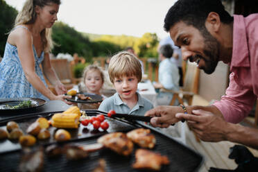 Ein Vater, der Fleisch und Gemüse auf dem Grill grillt, während einer Familien-Sommergartenparty. - HPIF10741