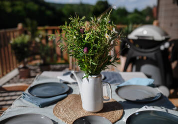 Ein Esstisch mit Blumenstrauß für das Abendessen auf der Terrasse mit Grill im Sommer, Gartenparty. Konzept. - HPIF10749