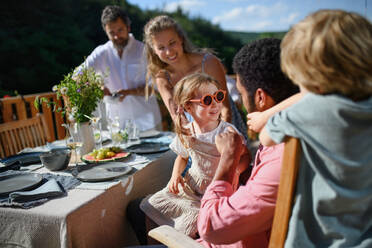 Eine Familie mit Kindern, die sich bei einer Grillparty auf der Terrasse amüsieren, Menschen, die am Tisch auf der Terrasse sitzen und sich unterhalten - HPIF10751