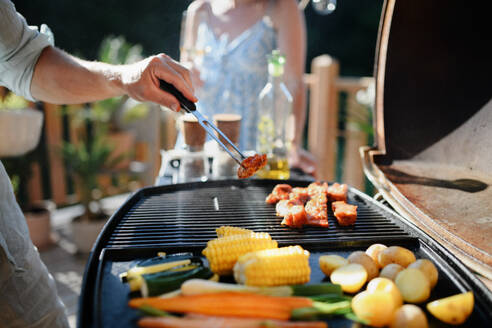 Ein unkenntlicher Mann grillt Rippchen und Gemüse auf dem Grill während einer Familien-Sommergartenparty - HPIF10756