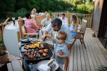 Ein Vater mit seinem kleinen Sohn grillt Rippchen und Gemüse auf dem Grill während einer Familien-Sommergartenparty. - HPIF10763