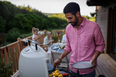 Ein Vater, der Fleisch und Gemüse auf dem Grill grillt, während einer Familien-Sommergartenparty. - HPIF10767