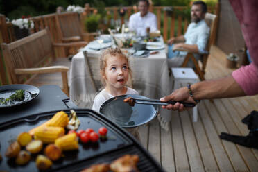 Ein Vater, der seiner Tochter während eines sommerlichen Familienfestes gegrilltes Fleisch und Gemüse auf den Teller legt. - HPIF10768