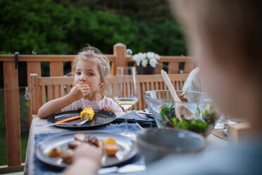 Eine Familie isst auf einer Grillparty auf der Terrasse, ein kleines Mädchen isst gerösteten Mais und genießt ihn. - HPIF10773