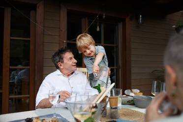 A little boy pouring lemonade to his grandfather during family celebration outside on patio. - HPIF10783