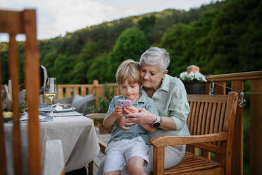 Kleiner Junge mit seiner Großmutter, der während einer Gartenparty in sein Smartphone schaut. - HPIF10785