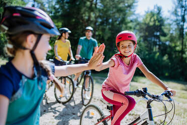 Eine junge Familie mit kleinen Kindern, die sich auf eine Fahrradtour vorbereitet, steht mit ihren Fahrrädern in der Natur und gibt sich die Hand. - HPIF10803