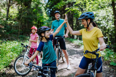 Eine junge Familie mit kleinen Kindern, die sich auf eine Fahrradtour vorbereitet, steht mit ihren Fahrrädern in der Natur und gibt sich die Hand. - HPIF10808