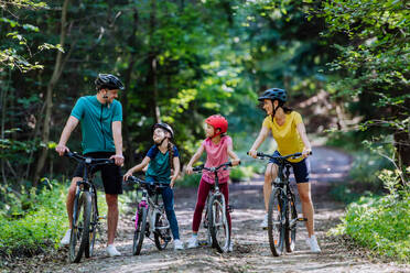 Eine junge Familie mit kleinen Kindern, die sich auf eine Fahrradtour vorbereitet, steht mit Fahrrädern in der Natur. - HPIF10812