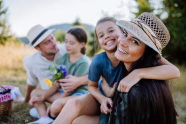 Glückliche Mutter und ihre Tochter umarmen sich beim Familienpicknick in der Natur, auf einer Decke sitzend. - HPIF10822