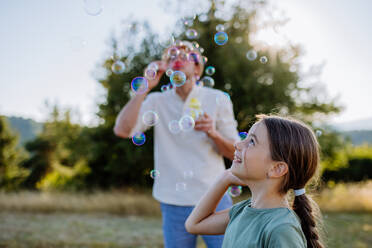 Ein junger Vater und seine kleine Tochter haben Spaß beim Seifenblasenblasen an einem Sommertag in der Natur. - HPIF10838