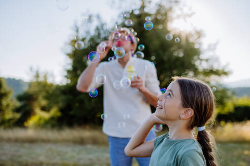 A young father and his little daughter having fun while blowing soap bubbles on a summer day in nature. - HPIF10838