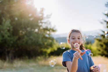 Kleines Mädchen hat Spaß beim Blasen von Seifenblasen an einem Sommertag in der Natur. - HPIF10842