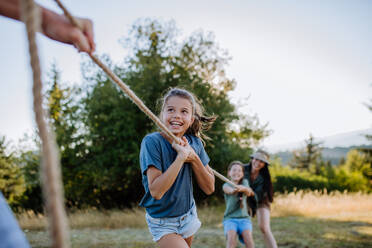 A young family with happy kids having fun together outdoors pulling rope in summer nature. - HPIF10846