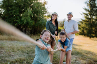 Eine junge Familie mit glücklichen Kindern, die sich im Sommer in der Natur beim Seilziehen vergnügen. - HPIF10848