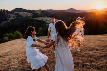 A happy young parents with daughters walking for picnic in nature in summer during sunset. - HPIF10872