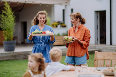Fröhliche Frauen bringen einen Salat und Burger zu einem Mehrgenerationen-Gartenfest im Sommer mit. - HPIF10887