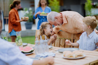 Eine Mehrgenerationenfamilie feiert eine Gartenparty, der Großvater unterhält die Enkel, lacht und hat Spaß. - HPIF10888