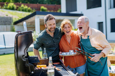 Ein älteres Ehepaar mit erwachsenem Sohn grillt draußen im Hinterhof während einer Gartenparty - HPIF10900