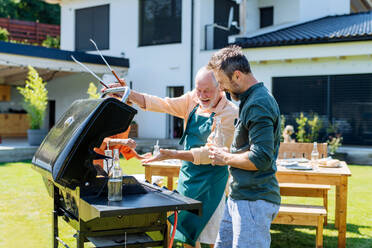 Ein älterer Vater mit erwachsenem Sohn grillt draußen im Hinterhof im Sommer Familie während Gartenparty - HPIF10905