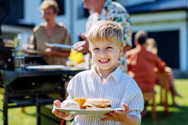 Ein fröhlicher kleiner Junge serviert Burger auf einem Mehrgenerationen-Gartenfest im Sommer. - HPIF10909
