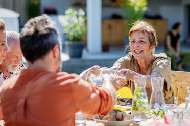 Eine Mehrgenerationenfamilie feiert ein Gartenfest, die Großmutter gibt ihrem Sohn einen Salat. - HPIF10911