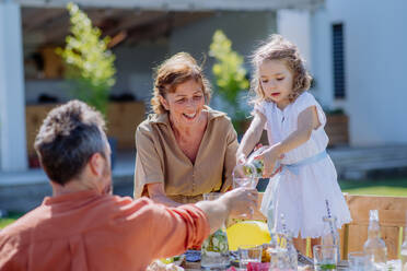 Eine Mehrgenerationenfamilie feiert ein Gartenfest, ein kleines Mädchen schenkt ihrem Vater Saft ein. - HPIF10913
