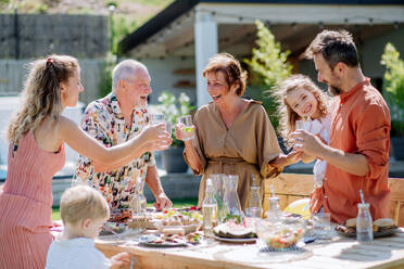 Eine Mehrgenerationenfamilie feiert eine Gartenparty, stößt an und lacht. - HPIF10914