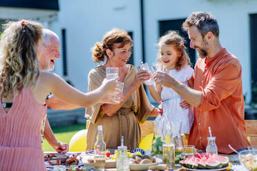 Eine Mehrgenerationenfamilie feiert eine Gartenparty, stößt an und lacht. - HPIF10915