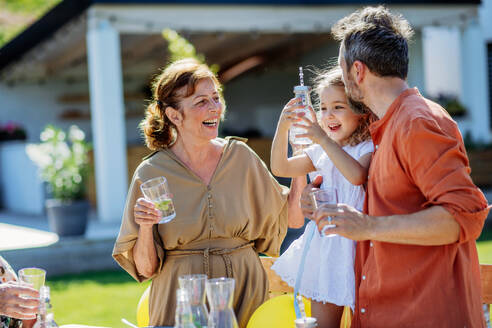 Mehr-Generationen-Familie mit Garten-Party-Feier, kleines Mädchen mit ihrem Vater und Großmutter trinken ein Wasser mit Zitrone, schöne Zeit haben. - HPIF10916