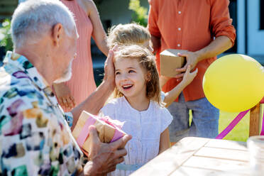 Ein glückliches kleines Mädchen, das ihrem älteren Großvater ein Geburtstagsgeschenk macht, bei einer Familiengeburtstagsfeier im Sommergarten - HPIF10922