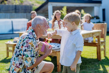 Ein glücklicher kleiner Junge, der seinem älteren Großvater ein Geburtstagsgeschenk macht, bei einer Familiengeburtstagsfeier im Sommergarten - HPIF10924