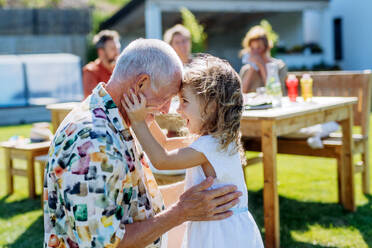 Happy little girl embracing her grandfather at generation family birthday party in a summer garden. - HPIF10925