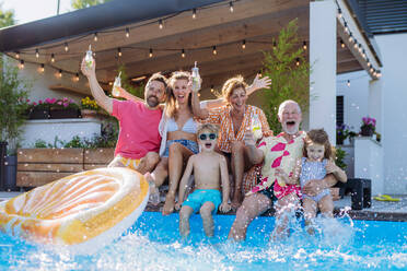 A multi generation family enjoying drinks and splashing when sitting at backyard pool. - HPIF10937