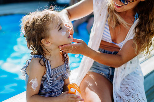 Junge Mutter, die ihrer Tochter eine Sonnenschutzlotion aufträgt. Sicherheit beim Sonnenbaden an einem heißen Tag. - HPIF10941
