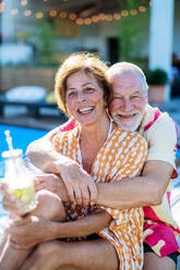 A happy senior couple enjoying drinks when relaxing and sitting by swimming pool in summer. - HPIF10948