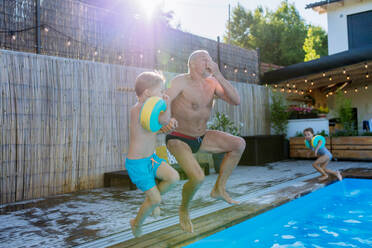 Ein Großvater mit seinem Granson, die Spaß zusammen haben, wenn sie in den Swimmingpool im Garten springen. - HPIF10952